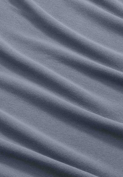 Primo piano di un tessuto grigio morbido e strutturato con pieghe diagonali che creano ombre e luci delicate.