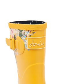 Botas de lluvia de goma amarillas con un patrón floral, textura antideslizante en la parte superior, detalle de hebilla ajustable y logo de la marca en el costado.