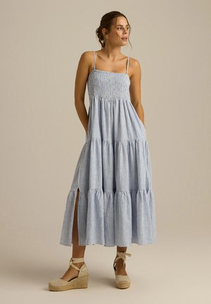 Niebieska i biała, w paski długa sukienka z marszczonym gorsetem, warstwową spódnicą, bocznymi kieszeniami i rozcięciami do ud. Połączona z espadrylami na koturnie.