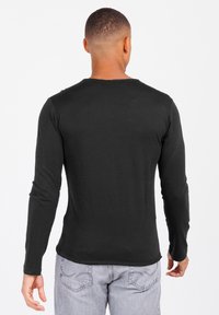 Schwarzes Langarm-T-Shirt aus weichem Stoff, mit Rundhalsausschnitt und geradem Saum, getragen mit hellgrauen Jeans.