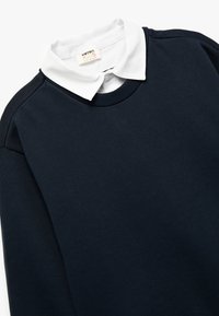 Sudadera de navy oscuro con un cuello de polo blanco, cuello acanalado y tejido texturizado. Diseñada para un uso casual con un ajuste relajado.