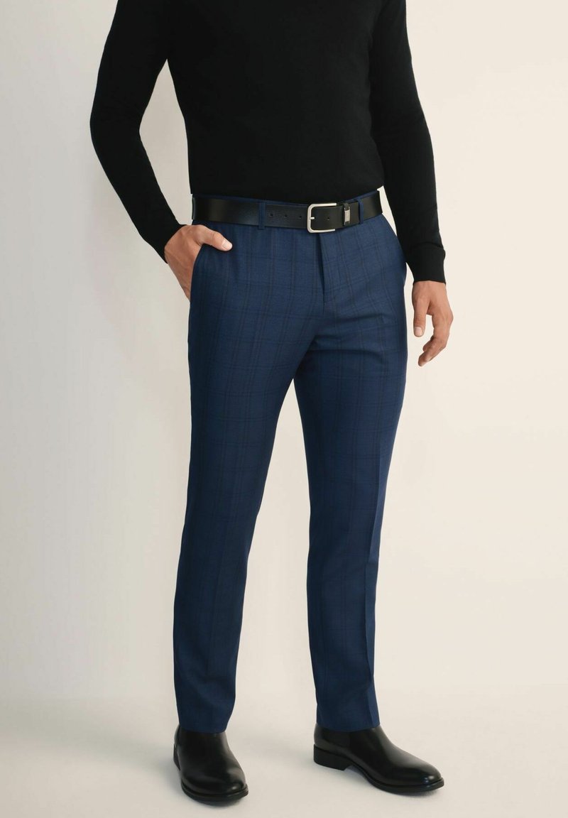 Granatowe spodnie w kratę o dopasowanym kroju, wykonane z teksturowanej tkaniny. Połączone z czarnym paskiem i eleganckimi czarnymi butami.