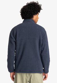 Pullover in pile navy con colletto alto, superficie testurizzata e orlo dritto. Presenta un dettaglio a yoke sulla parte superiore della schiena.