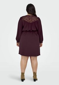 Burgundy klänning med långa ärmar och spetsdetalj på ryggen, med en åtsittande midja och en avslappnad passform, kombinerad med ankelstövlar.