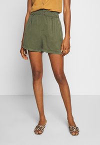 Olivgröna shorts med elastisk midja, med detalj i form av en knapp och en avslappnad passform. Matchas med leopardmönstrade slip-on skor.