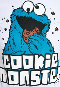 Blue Cookie Monster graphic on a white shirt, featuring large eyes, textured fur details, and the text "COOKIE MONSTER" in bold black font.
