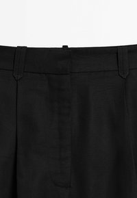 Pantaloni neri con una texture liscia, dotati di una vita su misura, due pinces frontali e una leggera lucentezza. Design minimalista senza hardware visibile.