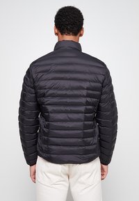 Czarna pikowana kurtka z ociepleniem, z kołnierzem stojącym i elastycznymi mankietami, widoczna od tyłu na jasnym tle.