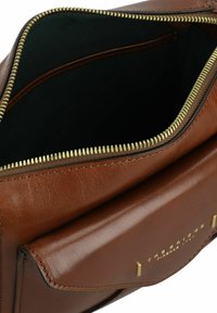 Braune Ledertasche mit Reißverschluss, goldenen Beschlägen, einem inneren grünen Futter und einer Außentasche. Minimalistisches Design mit klaren Linien.