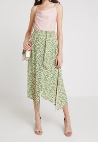 Blommig kjol i grönt och beige, med omlottmodell och hög slits. Matchas med en ljusrosa topp och accessoriseras med en liten vit väska.