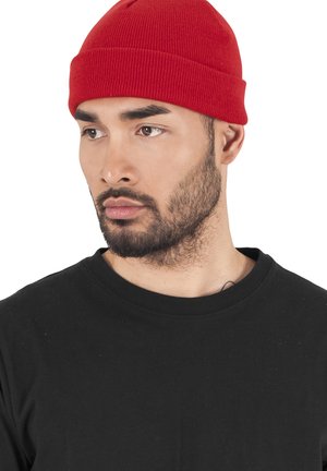 Red knit beanie on a person, featuring a textured ribbed design. Worn with a black t-shirt, emphasizing a casual style.