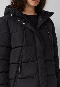 Schwarze Pufferjacke mit gestepptem Design, ausgestattet mit Kapuze, Reißverschlusstaschen und verstellbaren Kordeln. Glattes, wasserabweisendes Material.