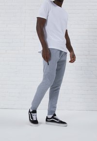 Grå sweatpants med en smal design och ribbade cuffs, i kombination med en åtsittande vit t-shirt och svarta och vita sneakers.