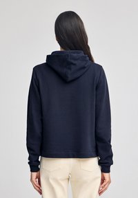 Felpa blu navy con cappuccio, maniche lunghe e design cropped. Texture liscia; presenta polsini e orlo a costine.