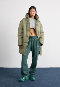 Abrigo acolchado verde oliva con capucha, top gris corto y pantalones de chándal verdes. Incluye detalles del logo de Nike, combinado con zapatillas verdes.