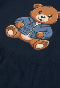 Marineblaues Gewebe mit einem Cartoon-Bären, der eine Jeansjacke trägt. Der Bär hat hellbraunes Fell und eine runde Form, mit gestickten Details.