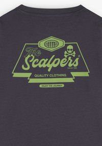 Tessuto grigio scuro con un logo grafico verde che presenta "The Scalpers", un emblema del globo, una testa di morto con le ossa incrociate e le frasi "Qualità dell'abbigliamento" e "Goditi il viaggio".