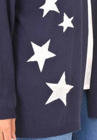 Námořnický pletený cardigan s velkými bílými hvězdami, žebrovanými manžetami a lemem, volným střihem a měkkou texturou.