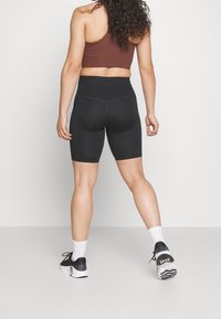 Pantalones cortos de bicicleta negros de cintura alta con una textura suave, combinados con una camiseta corta marrón y zapatillas deportivas negras con suelas blancas.