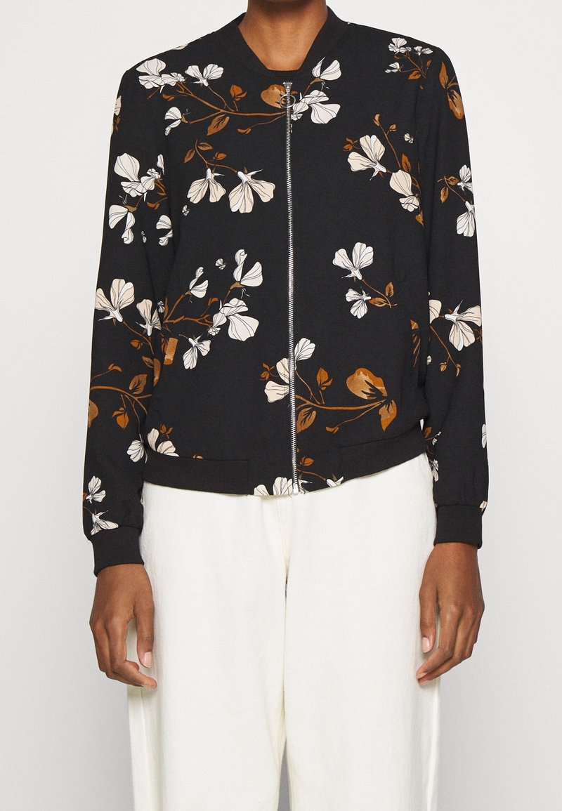 Chaqueta bomber negra con patrones florales en blanco y marrón, cierre de cremallera en la parte delantera, puños y dobladillo acanalados. Fabricada con un tejido suave.