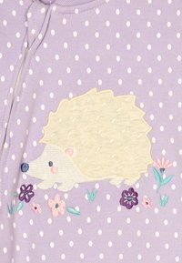 Lawendowa tkanina w białe kropki z haftowanym beżowym jeżem otoczonym różowymi i fioletowymi kwiatami.