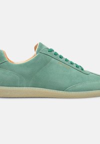 Sneaker verde in suede con una superficie liscia, caratterizzato da una punta arrotondata, lacci piatti e una suola in gomma beige. Design minimalista, senza motivi visibili.