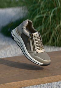 Světle šedý sneaker s texturovanou kůží a textilií, s bočním zipem, plochými šňůrkami a silnou bílou a černou podrážkou.