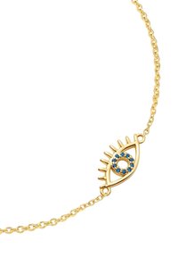 Auksinė grandinėlė su akies formos pakabuku, kuriame yra mėlyni stikliukai ir iškilūs blakstienų detalės, prieš minimalistinį foną.