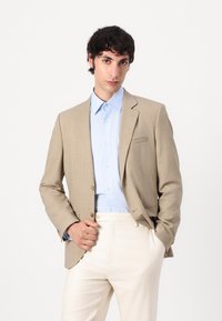 Beige blazer met een enkele knoop, lichtblauw overhemd met knopen en crèmekleurige broek. Gladde stof met een subtiel ruitpatroon.