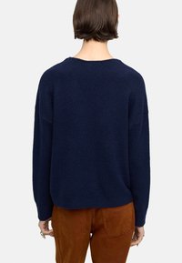 Granatowy, oversize sweter z teksturowanym splotem, okrągłym dekoltem i długimi rękawami, w połączeniu z brązowymi spodniami z kordurowej tkaniny.