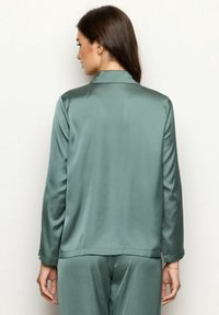 Satijnen groene pyjama set met een jas met lange mouwen, een sjaalkraag en een gladde textuur. Bevat een rechte zoom en minimalistische stikseldetails.