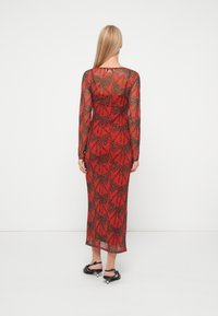 Czerwona sukienka z długim rękawem i przezroczystą narzutą, z czarnym wzorem motyli. Dopasowany krój o prostym fasonie i długości do kostek.