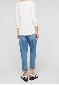 Vit långärmad topp, avslappnad passform; matchad med blå, löst sittande jeans och svarta sandaler med vita remmar. Enkelt, rent design.