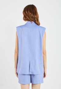 Ärmellose blaue Bluse mit vertikalen weißen Streifen, ausgestattet mit einem Reverskragen und einem Schlitz in der Mitte des Rückens, kombiniert mit passenden Shorts.