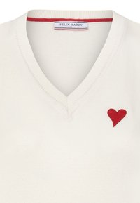 Witte V-hals trui met ribbels, met een kleine rode geborduurde hart op de linkerkant. De stof lijkt zacht en gestructureerd.