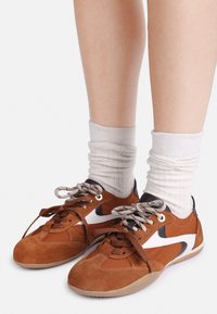 Brune semskede og syntetiske sneakers med hvite accenter, rund tå, og beige gummisåle. Snøring i en kontrastfarge. Hvit ankelsokker.