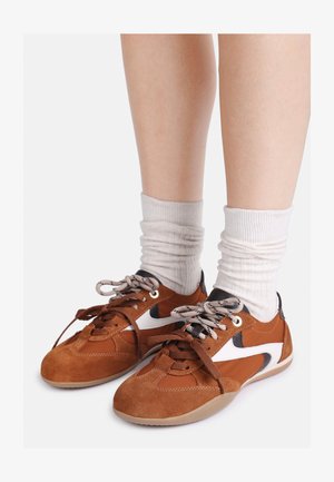 Barna velúrbőr és szintetikus sneakers fehér kiemelésekkel, lekerekített orral és barna gumitalppal. A fűzők kontrasztos színűek. Térdig érő fehér zoknik.