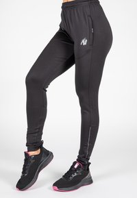 Svarta träningsleggings med en slimmad design, elastisk midja, sidofickor och en silverfärgad logotyp. Matchas med svarta och rosa skor.