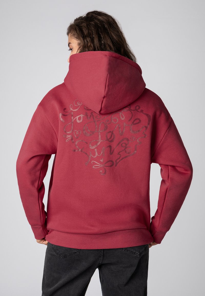 Rode hoodie met een groot bedrukt ontwerp op de achterkant, met decoratieve tekst en hartjes in een contrasterende kleur. De stof heeft een zachte textuur.