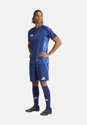 Blauw voetbaltenue gemaakt van ademend materiaal; heeft korte mouwen, een gemusterde zijkant en witte Adidas-logo's; gecombineerd met zwarte voetbalschoenen en blauwe sokken.