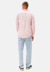 Camisa de manga larga a rayas rosas claras con cuello abotonado, combinada con jeans azul claros y zapatillas negras, vista desde la parte de atrás.