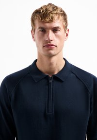 Marineblauwe pullover met een ritskraag, gemaakt van een gladde stof. Kenmerkt zich door raglanmouwen, een aansluitend ontwerp en geen zichtbare patronen of logo's.