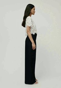 Fehér csipkés, rövid ujjú cropped top, amelyet magas derekú fekete nadrággal párosítottak, sima textúrával és karcsú siluettel.