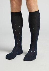 Calcetas hasta la rodilla en azul marino con una textura suave, que presentan pequeños patrones cuadrados en turquesa distribuidos de manera uniforme.