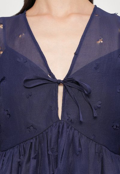 Vestido azul marino en tela transparente con bordado floral, escote en V, detalle de lazada en el centro y cintura fruncida.