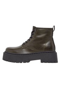 Bottine en cuir vert olive avec une épaisse semelle à plateforme noire, devant lacé et tirant à l'arrière, avec une texture lisse et un design minimaliste.