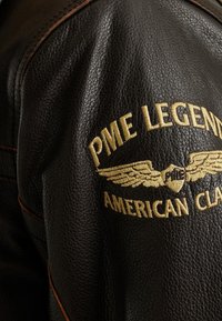 Svart läderjacka med texturerad finish, som har guldbroderi med "PME Legend American Classic" och accenter av vingemblem.