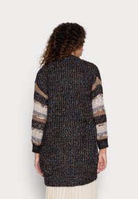 Sweter kardigan z kolorowymi wzorowanymi rękawami w odcieniach beżu i brązu, z ciemnym, teksturowanym korpusem, długości do pasa, z prążkowanym wykończeniem.