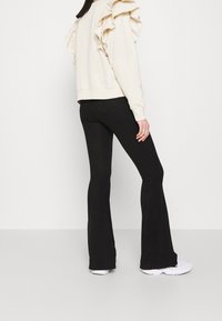 Ljust beige sweatshirt med volangärmar, parat med svarta ribbade utsvängt byxor. Outfiten inkluderar vita sneakers för kontrast.