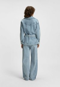 Denim jacket with a belted waist, light blue color, larger collar, and back yoke detail; paired with wide-leg light blue jeans.